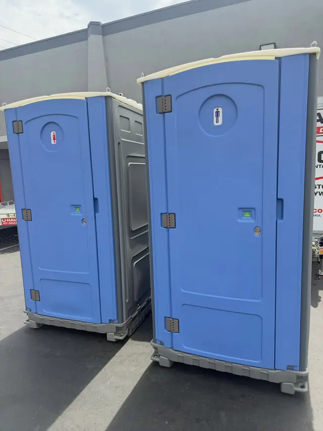 Two blue porta potties on a paved lot
