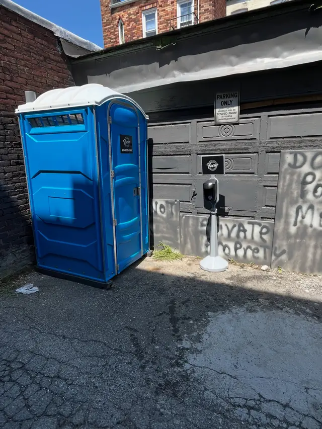 Blue porta potty placed on pavement beside a building