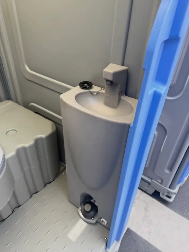 Foot-pump hand sink with soap dispenser inside a gray deluxe porta potty