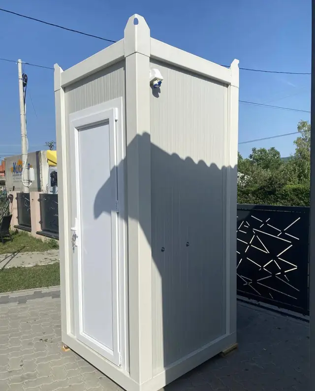 White flushing restroom cabin with a single door standing on a paved driveway