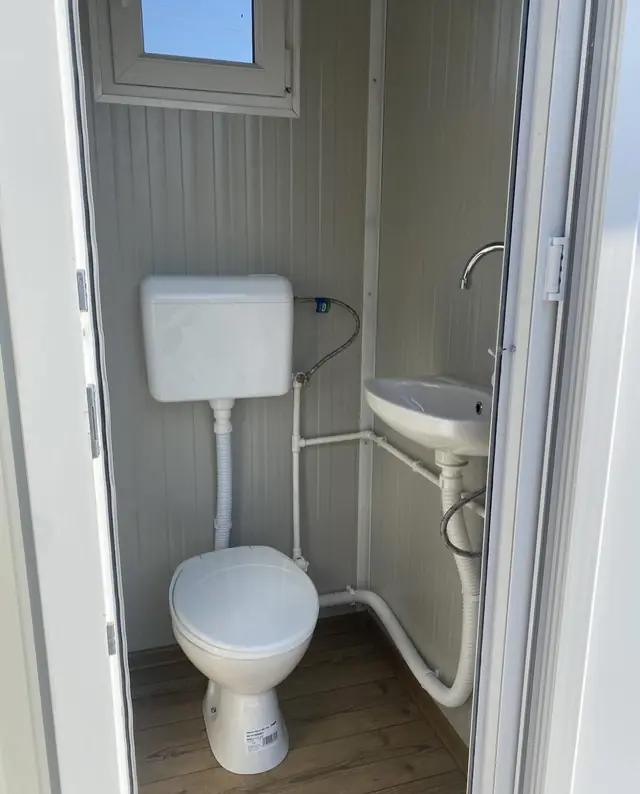 Inside a flushing restroom cabin with a white flush toilet, tank and small wall sink