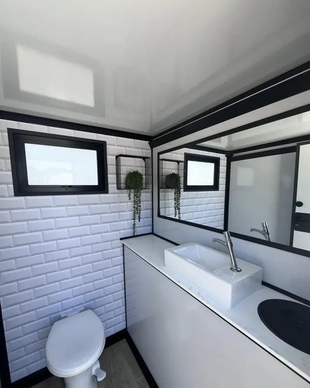 Inside a restroom trailer stall with white brick walls, vessel sink and flush toilet