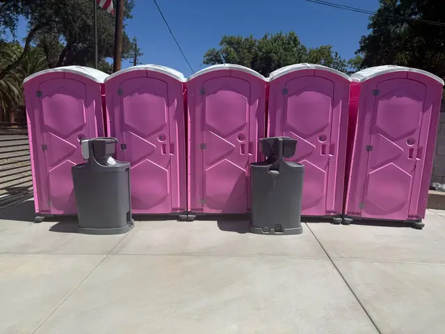 Pink porta potties with hand-wash stations at an event