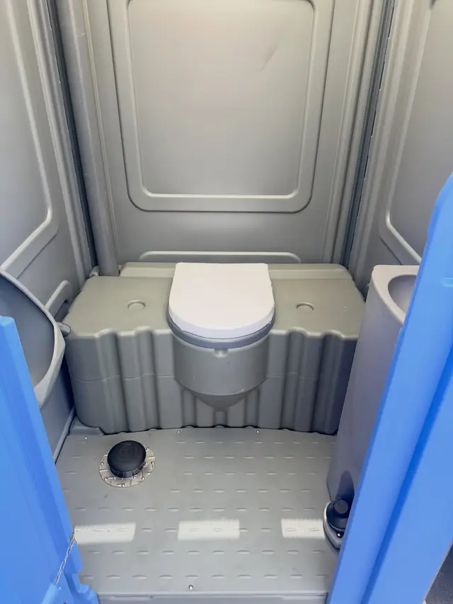 Gray toilet seat and textured floor inside a standard porta potty