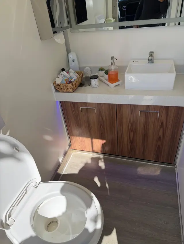 Restroom trailer vanity with wood cabinet, white sink and amenity basket