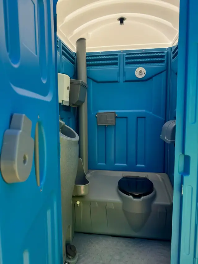 Inside a blue standard porta potty showing the urinal, toilet seat and toilet paper holders