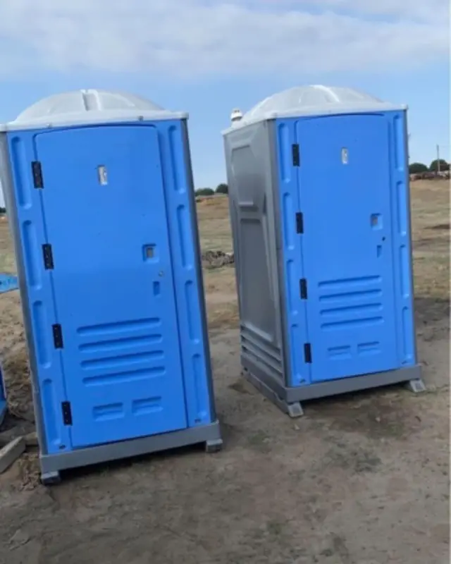 Two blue standard porta potties on a job site